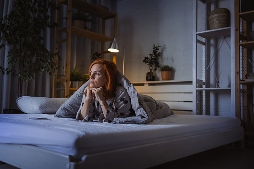Sad mid adult woman lying in bed and looking away