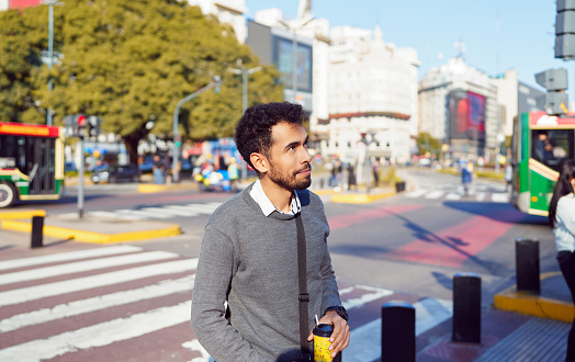 portrait young latin american businessman walking down the street crossing the zebra crossing through the city center
