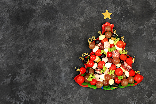 Christmas and New Year's dishes, a set of snacks for the festive table. Plate with herringbone canapÃ©s of tomatoes, pate, mozzarella cheese, salami, olives, black olives and grapes on a concrete table, selective focus