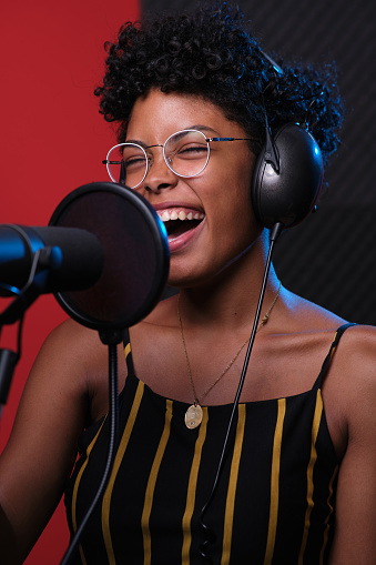 Close-up of an African woman singing in front of a recording studio microphone with headphones on and eyes closed.