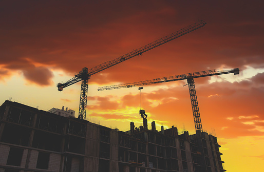 Construction site with building construction on sunset. Tower cranes in action. Housing renovation and real estate. Crane during formworks. New Housing and residential buildings construction.