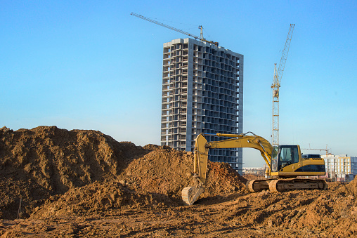 Excavator on groundwork on construction site. Backhoe dig foundation for house construction. Excavation works on building    construction. Excavator Machinery on earthworks. Tower crane in build.