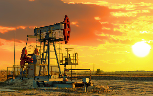 Oil prices on global market. Crude oil Pumpjack on oilfield on sunset.