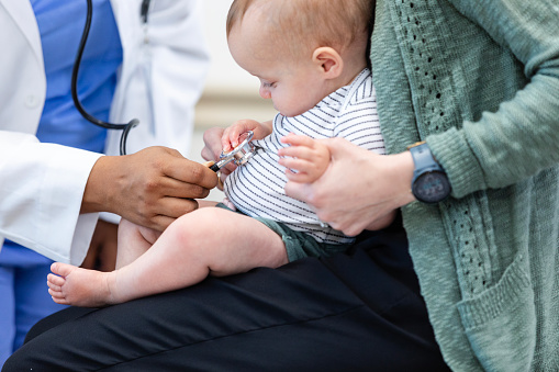An unrecognizable female pediatrician listens to the little baby's stomach with her stethoscope.