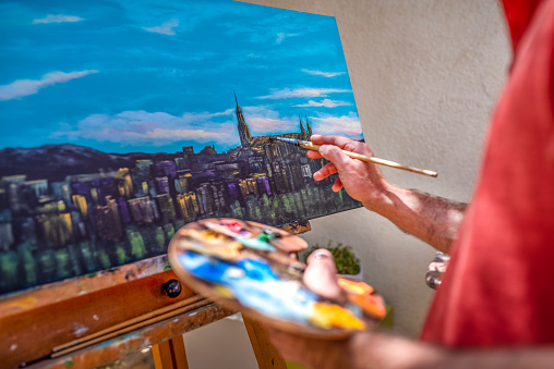 photo of male artist holding the color palette while paint on canvas