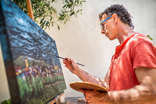 side view of a male artist painting on canvas at his studio