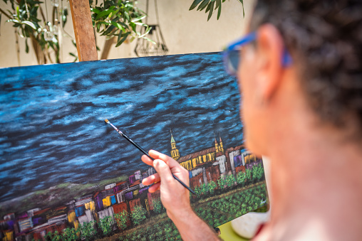 rear view of a male artist painting on canvas at his studio. Selective focus on the canvas