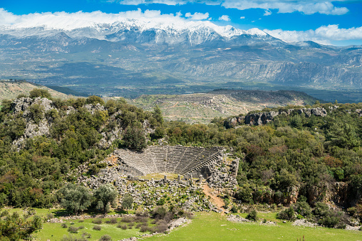 Landscape at Pinara ancient site in Mugla province of Turkey with a ruined amphitheatre and snow-covered mountains in the background. The amphitheatre dates to about 4th century BC. Pinara was a large city of ancient Lycia.