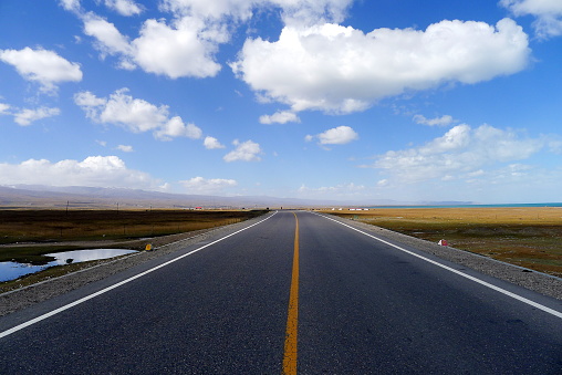 This picture shows a highway in plateau grassland and beautiful sky with white clouds.