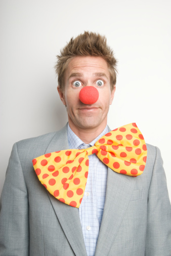 A male clown with a red nose smiles and holds a balloon in his hand. The clown gives a balloon to a girl 5 years old. Copy space.