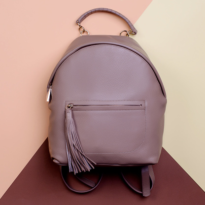 Modern brown leather backpack for women with a handle and a zippered pocket with a tassel pull isolated on a creative multicolor background. Elegant fall accessories. Outlet marketing poster.