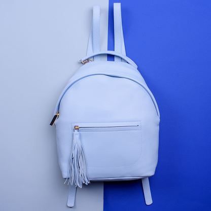 Fashionable women's light blue leather backpack featuring a top handle and a zippered pocket with a tassel pull isolated on a contrasting two-tone background. Fashion blogger content. Outlet poster.