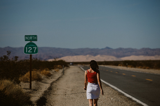Woman enjoying the vast wilderness of Death Valley, taking a quick break from driving, walking next to the empty road.