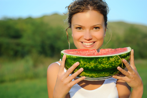 Young attractive woman eating watermelon in green grass, outdoors.