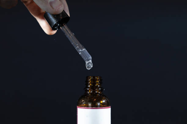 黒い背景に化粧品や医薬品に使用されるガラス瓶の上にピペットを持つ手の選択的なぼかし。半透明液体の泡がピペットに見えます。 - translucid ストックフォトと画像