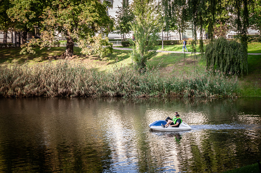 Picture of the pilsetas kanals in the Bastejkalns Park of Riga, Latvia with two men on a pedalo. Bastejkalns Park is a spacious park on the eastern edge of the old town of Latvian capital Riga.
