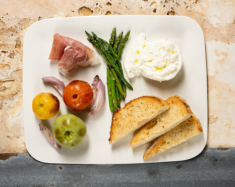 Appetizer plate above view with poached egg, prosciutto, onions, asparagus, bread, tomatoes on an above view