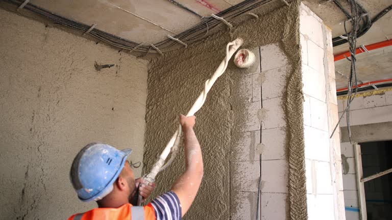 Construction worker, spraying plaster on a wall, while working on a construction site