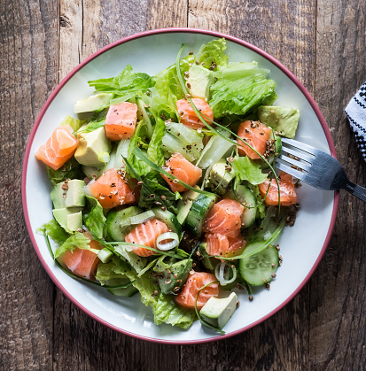 Fresh salmon salad with cucumbers, avocado, lettuce, arugula, white onions, pepper in bowl on wooden table