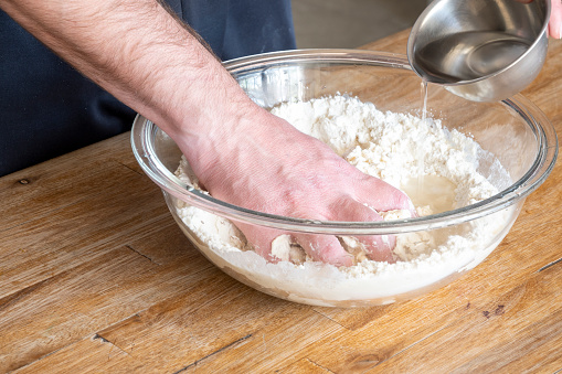 Man's hands kneading dough inside a glass bowl.