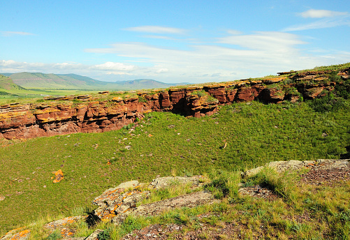 Wide rows of red sandstone stone formations running along the gentle slopes of a high hill on a sunny summer day. Mountain range Chests, Khakassia, Siberia, Russia.
