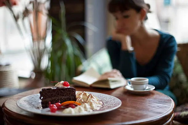 Young woman reading a book in a cafeteria, having coffee and chocolate cake