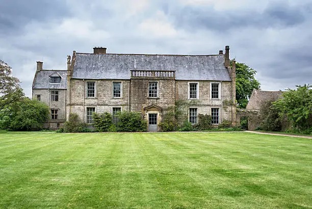 A large country manor dating from the 16 hundreds with large lawns and overhanging rainclouds.