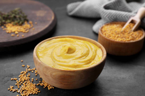 istock Bowl with delicious mustard and seeds on black textured table, closeup 1745760364