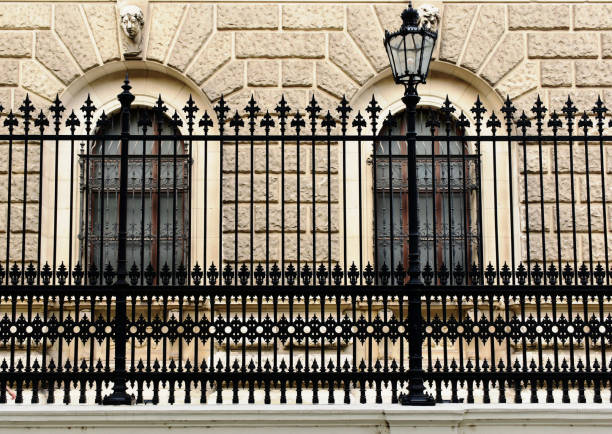 decorative black cast iron picket fence detail. front view along sidewalk at the Burggarten in Vienna, Austria. classic arched windows. European travel and tourism concept. ornate design and pattern. stucco elevation