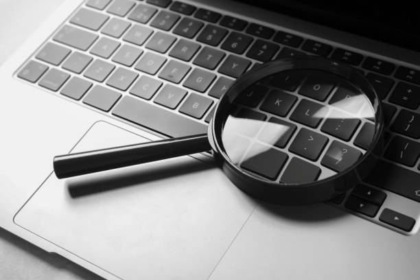 istock Magnifying glass and laptop on light grey table, closeup 1745838360