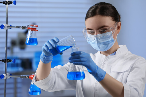Woman scientist experimenting with chemicals in lab. Lab technician doing research on new chemicals in laboratory, adding solution in conical flask.