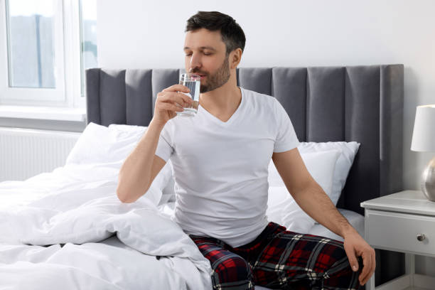 istock Handsome man drinking water from glass on soft bed at home in morning 1745863313