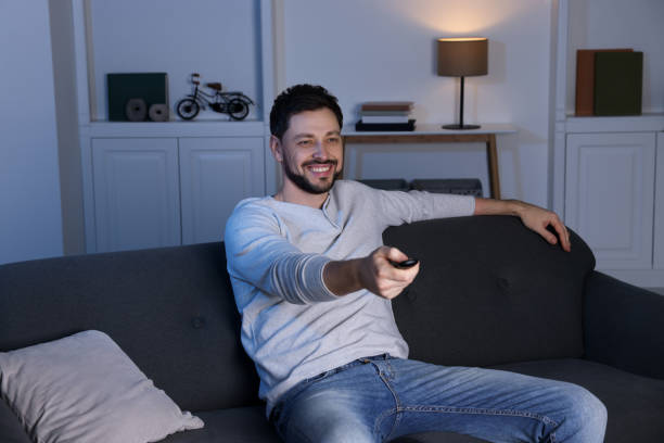 istock Happy man changing TV channels with remote control on sofa at home 1745872337