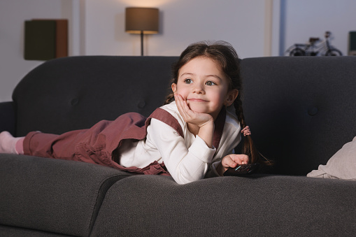 Cute little girl watching TV on sofa at home