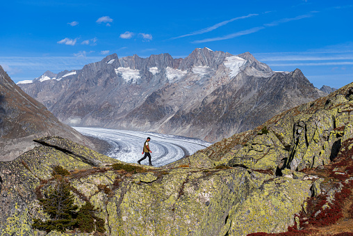 Side view of a solo man hiking the scenic ridge  of a rocky mountain in front of the glacier, Aletsch glacier, UNESCO World Heritage Site, Valais Canton, Switzerland