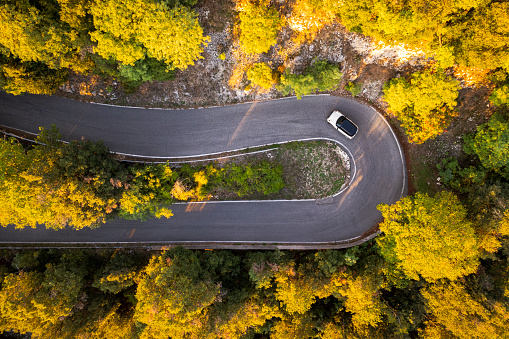 Top down aerial view of a car driving the hairpin curve crossing the forest in the autumn colors, Italy