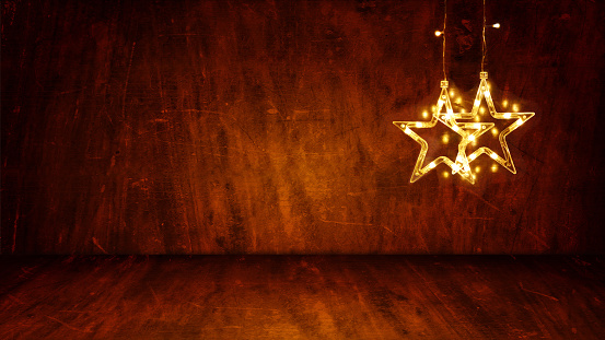 Dark brown colored wooden textured 3D or three dimensional horizontal blank Xmas or Diwali celebrations festive background, poster or wallpaper. Can be used as Christmas party wallpaper, backdrop, celebration, festive background, gift wrapping sheet. There are two stars lights hanging from the top of a wall leaving plenty of copy space.