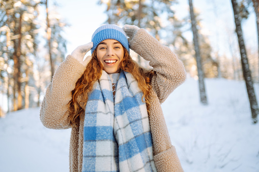 Waist up portrait of happy young woman posing outdoors in winter standing under beautiful pine trees, copy space