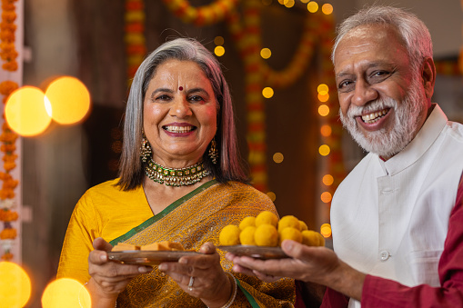 Senior couple holding sweets and celebrating Diwali festival together at home