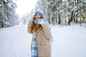 Smiling woman in a winter snow-covered park walks and plays with snow.