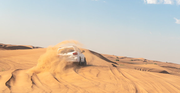 Dubai, United Arab Emirates, March 20, 2023 : White closed jeep Toyota extremely drives through the sandy desert near Dubai city, United Arab Emirates