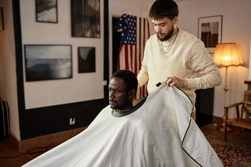 Professional barber covering the customer and working with him in barber shop