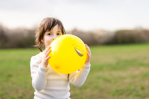 Cute girl holding a yellow balloon and looking at camera. Copy space