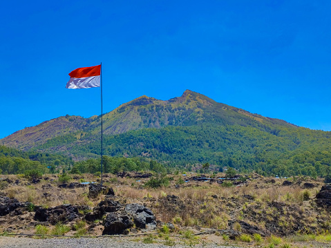 Indonesia flag waving with the background of Mount Batur, Kintamani, Bali, Indonesia during the daylight in dry season.