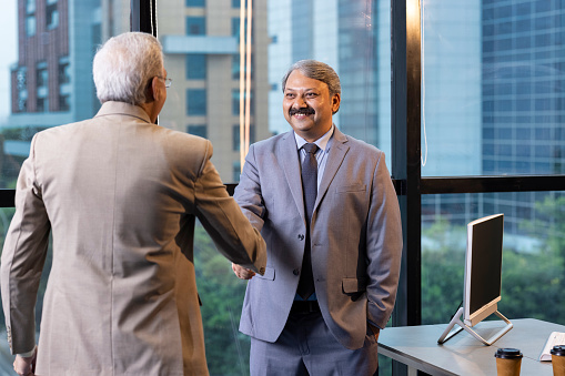 Two smiling businessmen shaking hands while standing in an office.