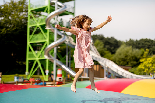 Little girl jumping on inflatable trampoline, having fun visiting amusement park during a summer vacation