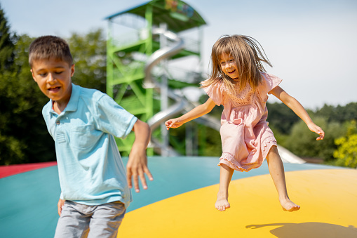 Kids jumping on inflatable trampoline, having fun visiting amusement park during a summer vacation. Brother with a sister spending leisure time together