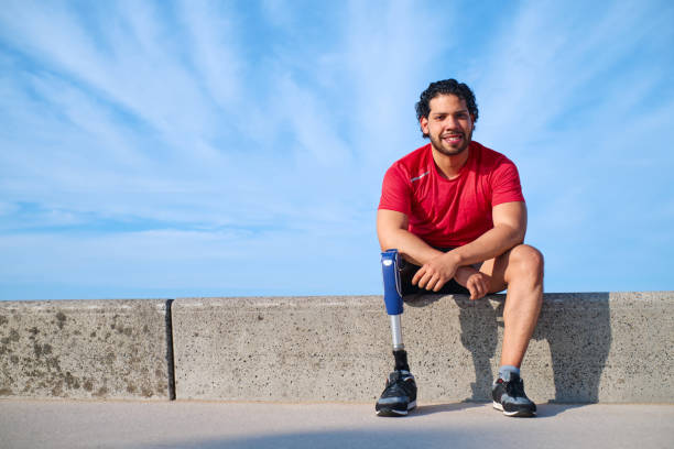 istock Young man with a prosthetic leg sitting on a retaining wall in the beach looking at camera 1746069164