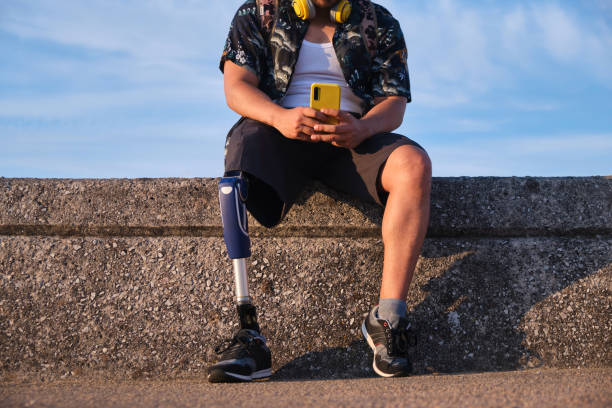 istock Unrecognizable young man with a prosthetic leg sitting on retaining wall near beach using phone 1746069788