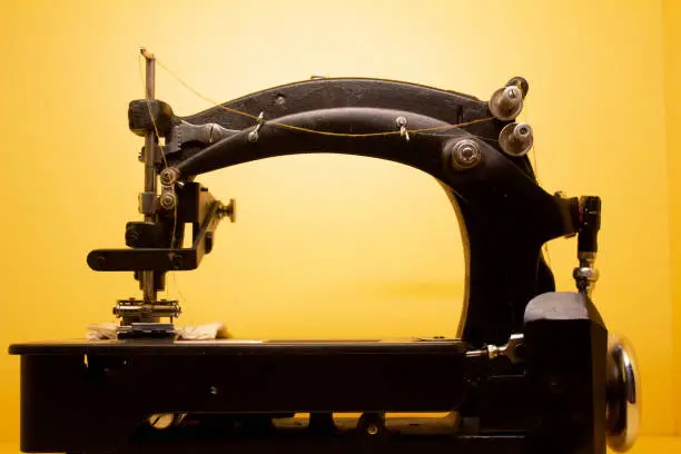 very old black sewing machine from the year 1900 with sewing thread and yellow background